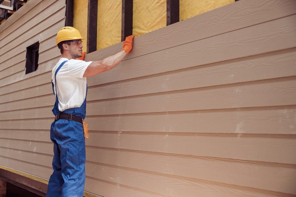 Handsome young man construction worker wearing safety helmet and work overalls while installing wood siding