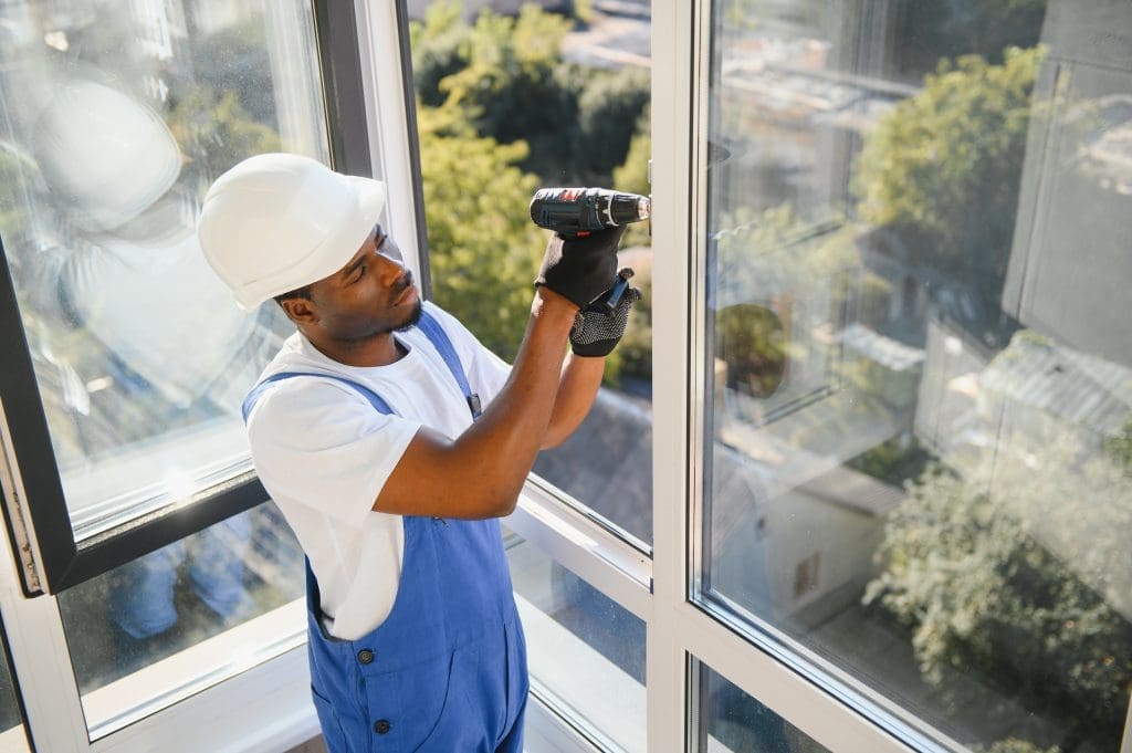 Workman in overalls installing or adjusting plastic windows in the living room at home