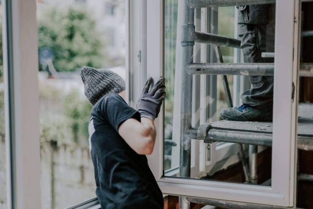 One young handsome Caucasian man in a black construction uniform stands sideways and helps his partner install a window frame in the house, close-up side view. Concept for home renovation and window installation.